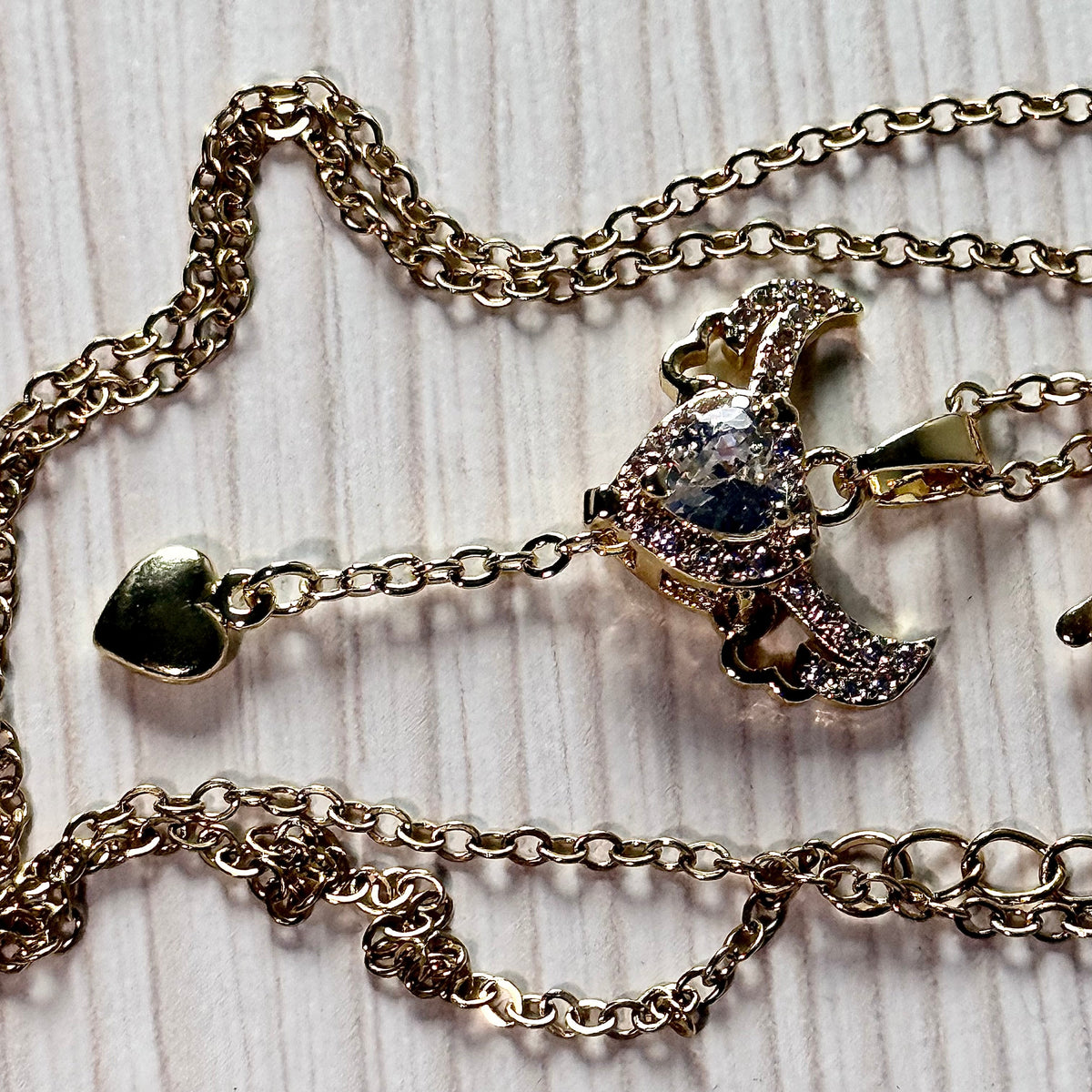 Gold winged heart necklace chain detail flat lay on white surface