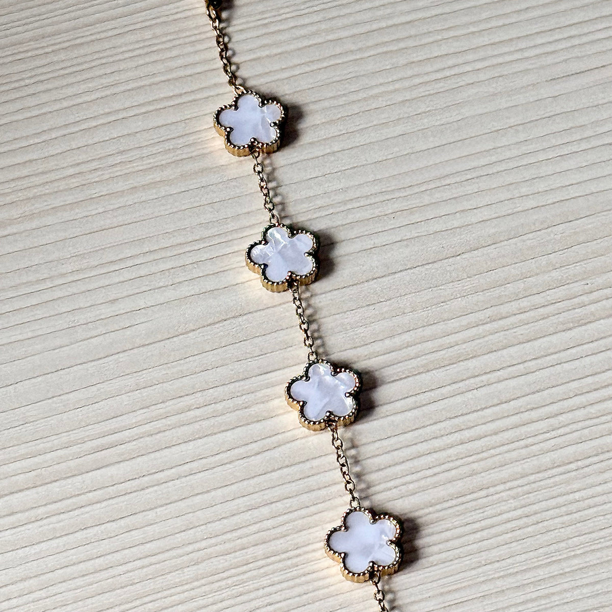 Gold clover charm bracelet close-up showing 5 white clover charms