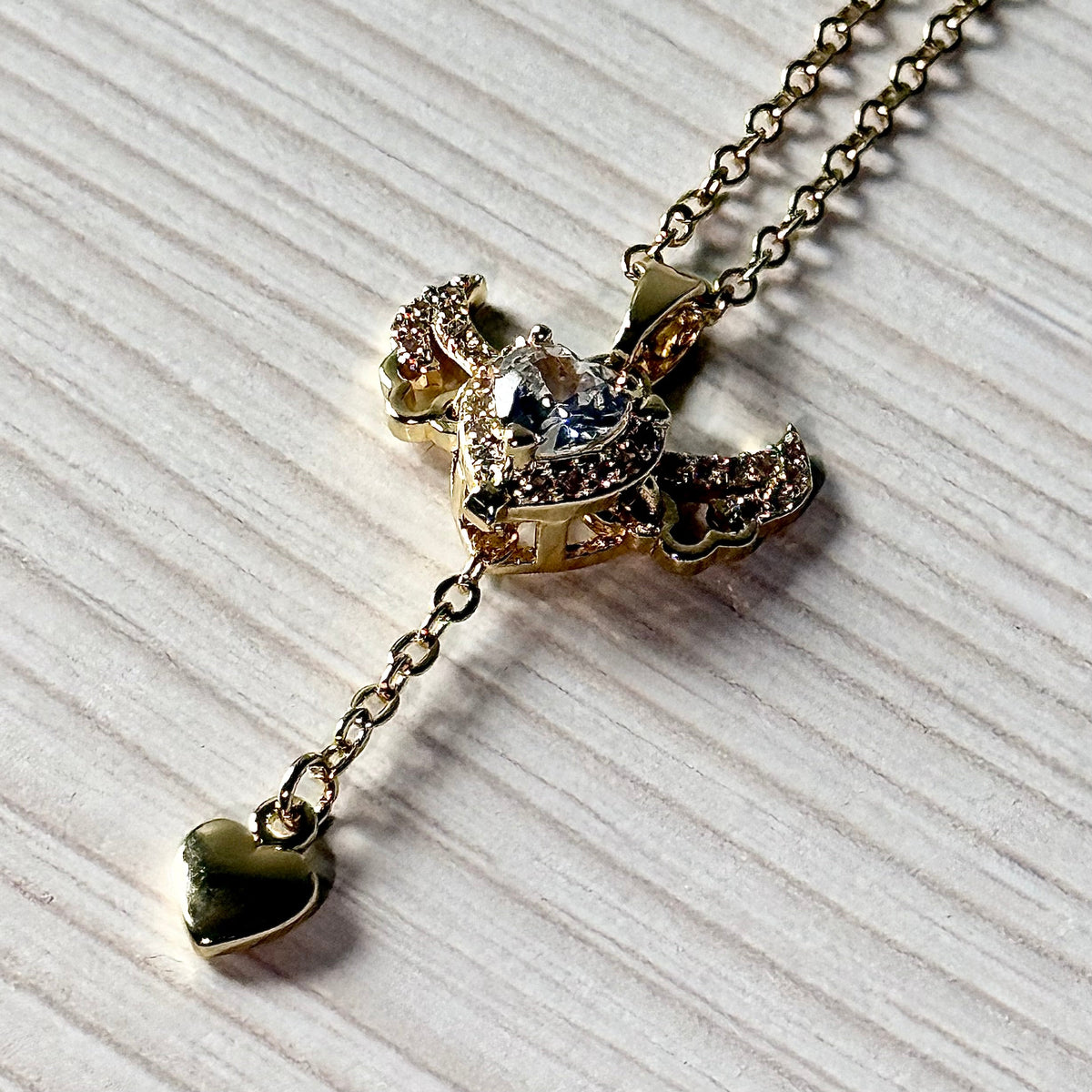 Gold winged heart pendant necklace with dangling heart charm on white surface