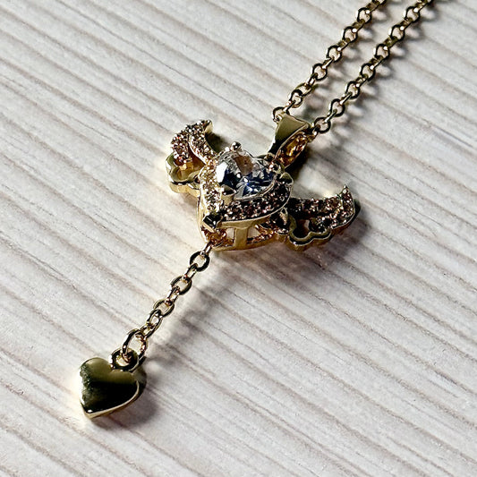 Gold winged heart pendant necklace with dangling heart charm on white surface