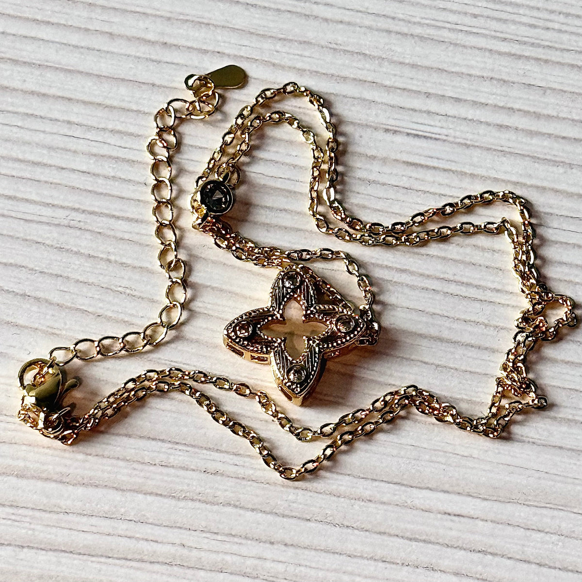 Gold filigree flower pendant necklace full chain flat lay on white surface