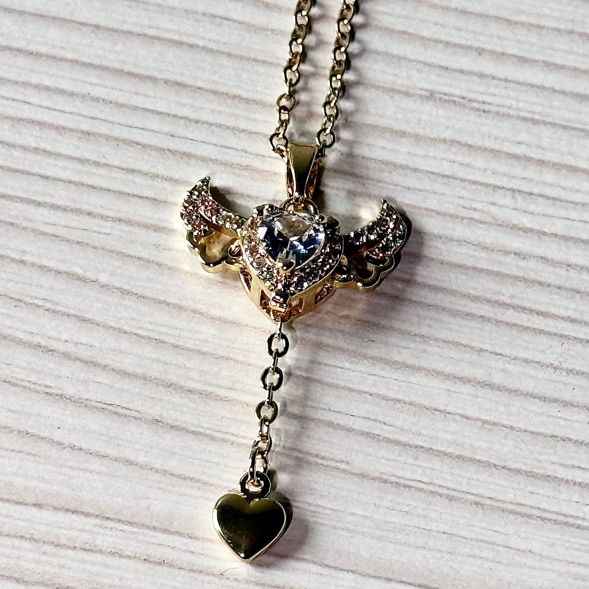 Gold winged heart pendant necklace close-up showing crystal pavé and CZ stone