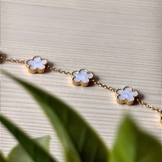 Gold clover charm bracelet with white mother-of-pearl charms on marble